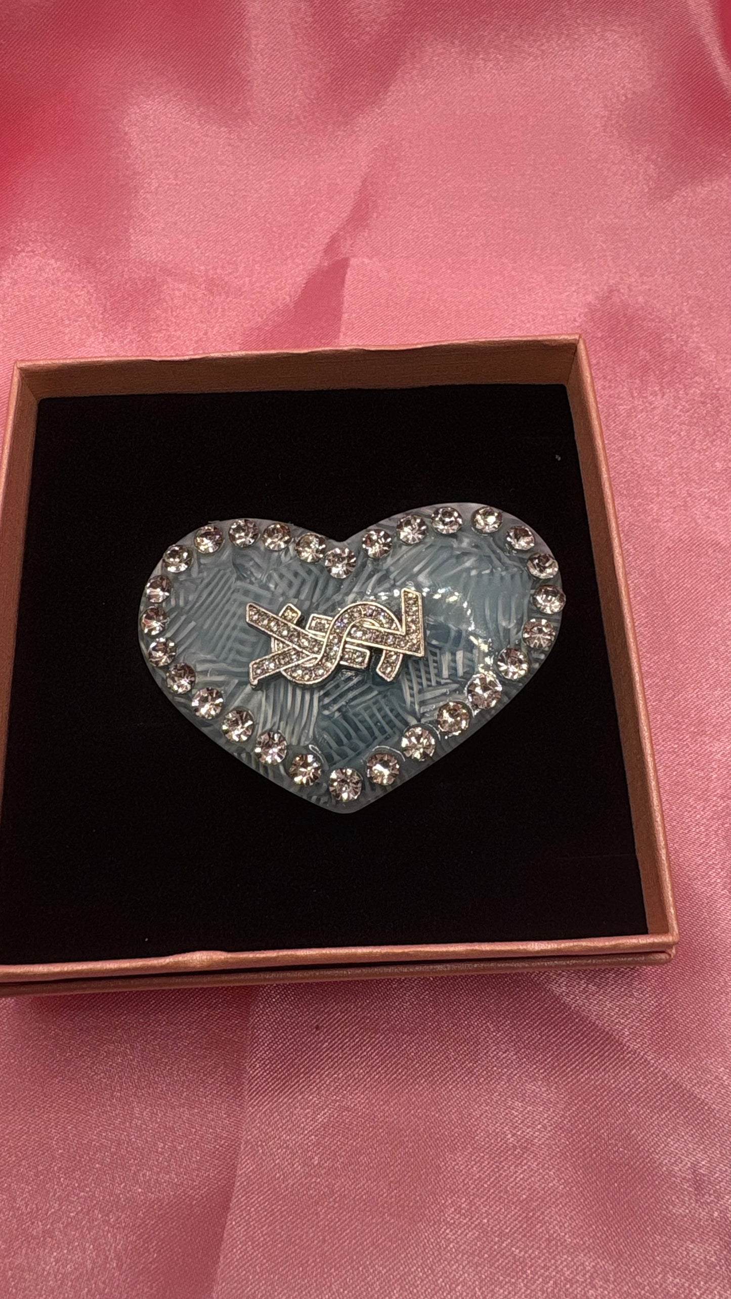 Heart-shaped hair clip with rhinestones in a box on a pink fabric background
